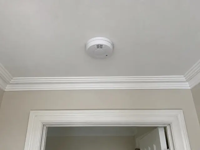 Ceiling smoke alarm above a doorway in a beige room with white cornices in Crows Nest